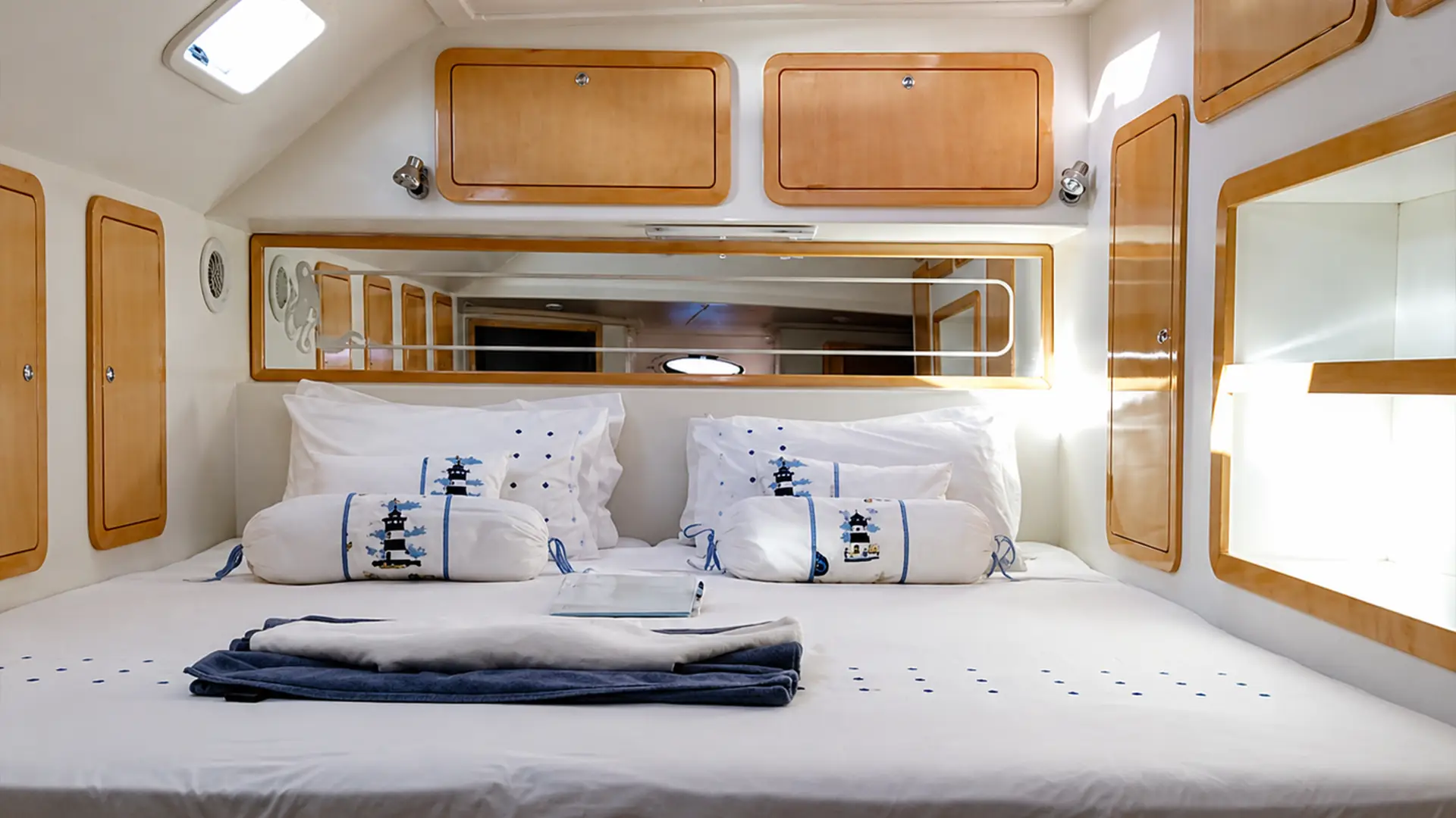 Bed with white and blue lighthouse-themed pillows and wooden cabinets in a compact cabin space.