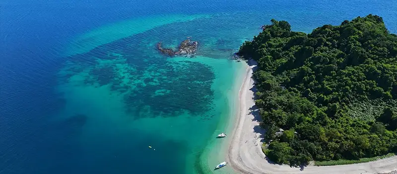 Aerial view of a tropical island with dense greenery, white sandy beach, and turquoise surrounding waters.
