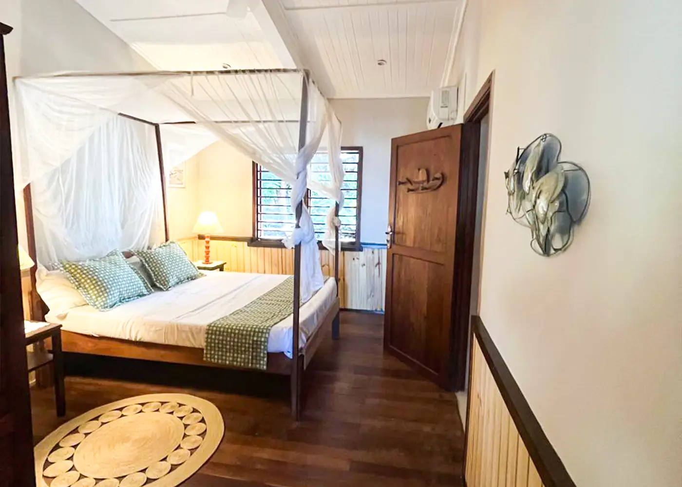 Cozy bedroom with four-poster bed, green checkered pillows, wooden floor, and bedside lamps lit.